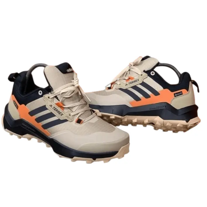 Pair of rugged trail sneakers in beige with orange and navy accents, featuring a thick grip outsole and cushioned sole designed for outdoor and all-terrain use.