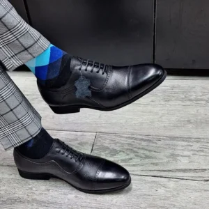 Men’s genuine leather black formal shoes with lace-up design and rubber sole, worn with tailored trousers for a professional look.
