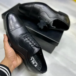 Men’s genuine leather black formal shoes with lace-up design and rubber sole, worn with tailored trousers for a professional look.